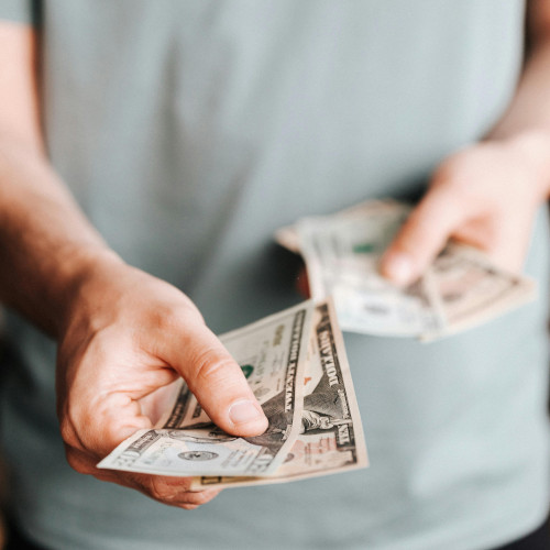 A male nurse in scrubs holding out twenty dollar bills